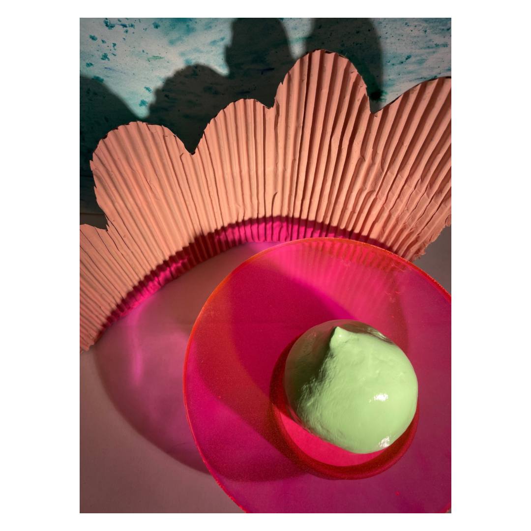 Assemblage: a green glazed form on a pink perspex disc, in front of a scalloped terracotta fan